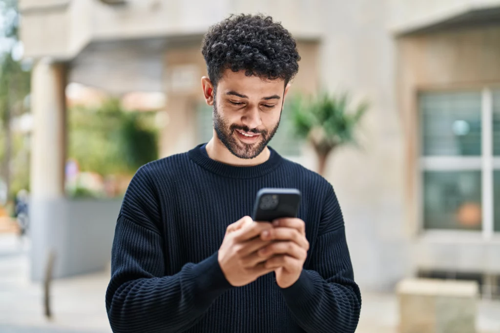 A person with curly hair and a beard, smiling while looking at their phone, perhaps reviewing Patient Info at Laughlin Dental