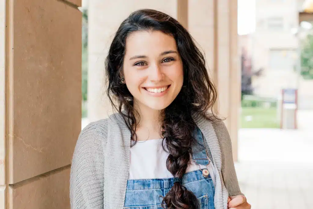 A smiling young woman with dark, braided hair, potentially exploring Dental Bridges at Laughlin Dental