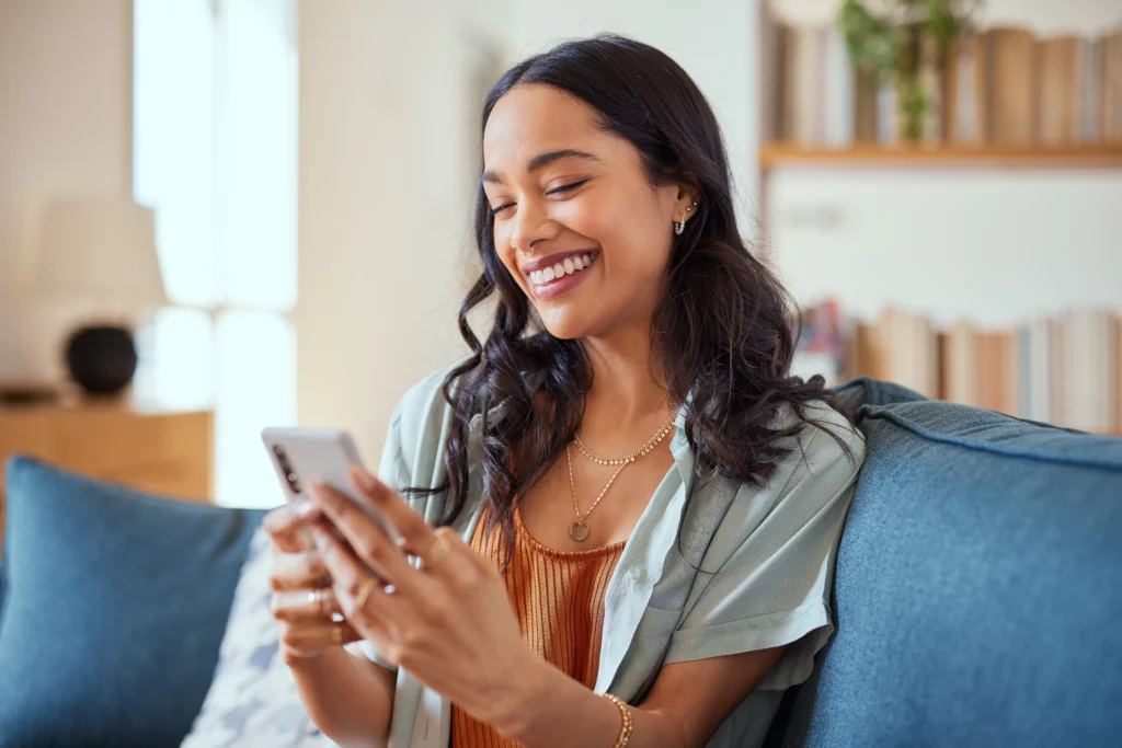 A person with long, dark hair smiles while looking at their phone, perhaps reviewing the Privacy Policy at Laughlin Dental