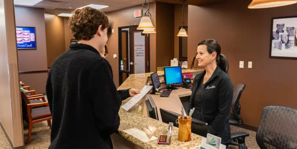 A smiling receptionist assisting a patient at the front desk of Laughlin Dental