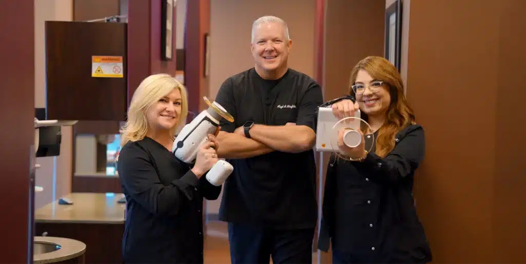 Three smiling dental professionals, two holding X-ray devices, showcasing their team at Laughlin Dental