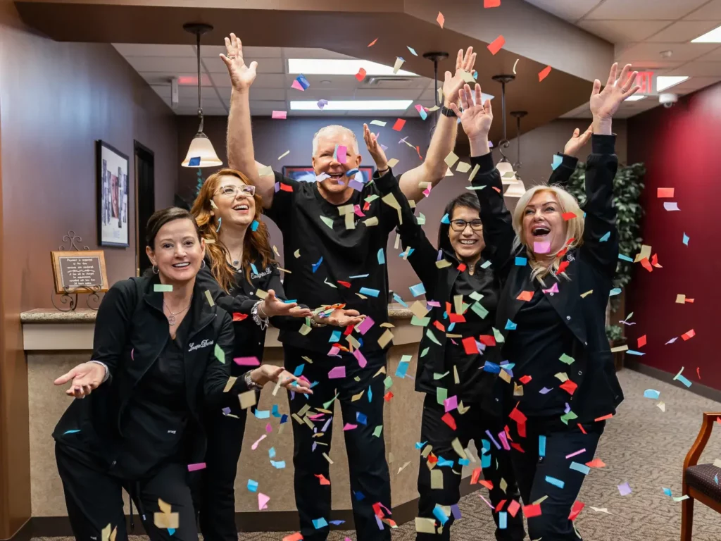 Five cheerful dental professionals at Laughlin Dental celebrating with confetti falling around them