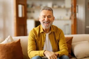 man smiling on the couch in a yellow shirt. dental implants in pasadena tx